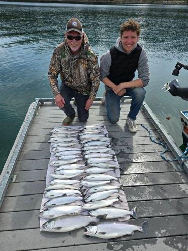 Two men kneeling on a dock with a large catch of fish laid out.