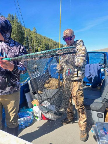 Two men on a boat holding a fishing net with a fish inside.