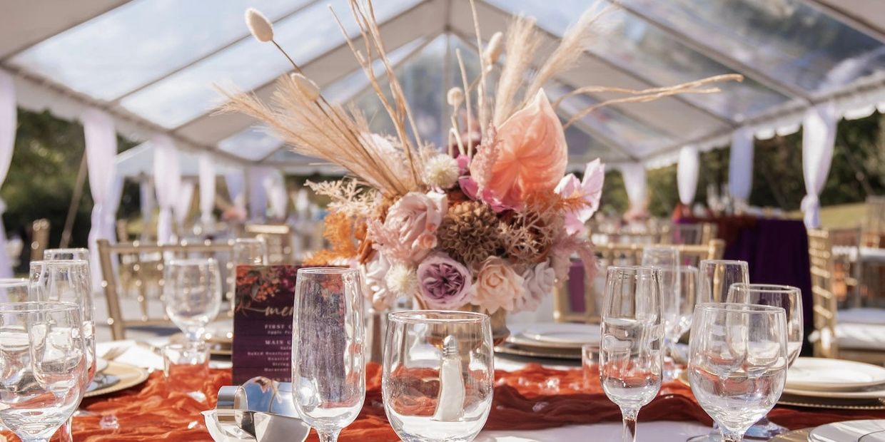 Elegant table setting with floral centerpiece under a clear tent.