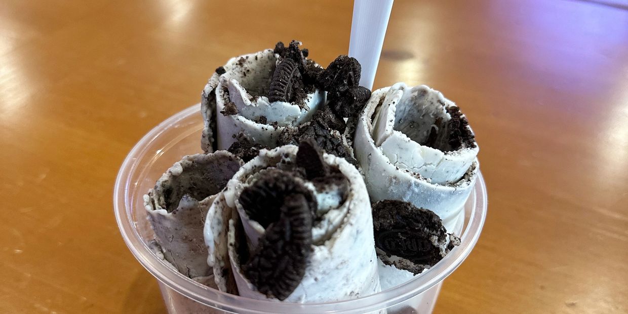 Rolled ice cream with Oreo cookies in a clear plastic cup on a wooden table.