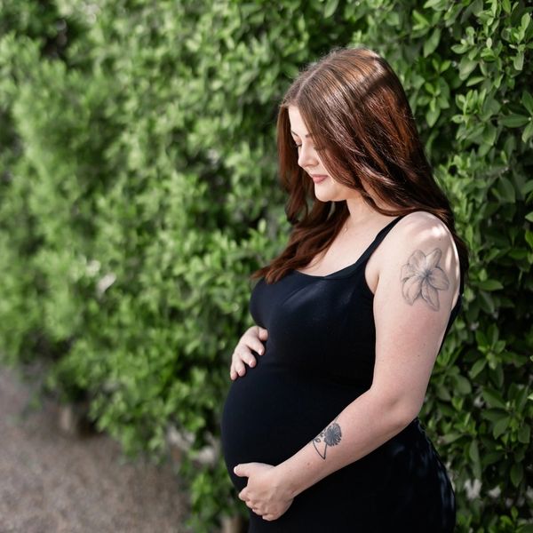 A pregnant woman cradling her bump in front of trees.