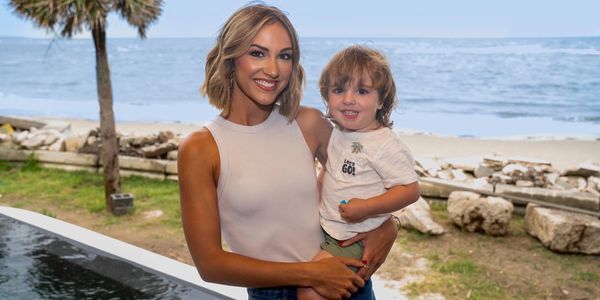 A woman holding a smiling toddler near the beach.