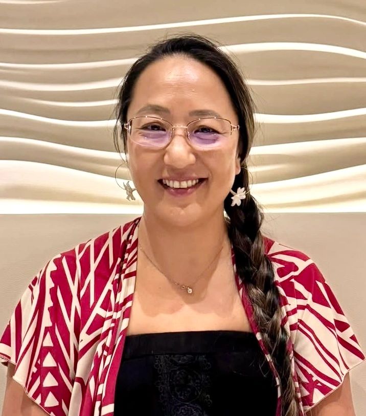 Smiling woman with braided hair and glasses, wearing a patterned red and white shawl.