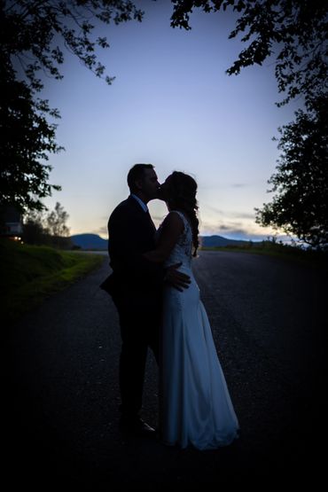 Silhouette of a couple kissing at twilight on a quiet road.