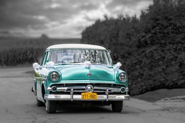 A vintage green and white car parked on a road with blurred background.