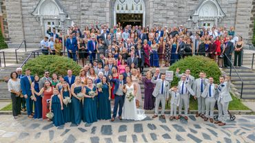 Large wedding party posing on church steps for a group photo.