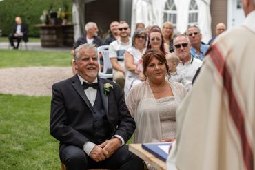 An elderly couple smiling during an outdoor wedding ceremony.