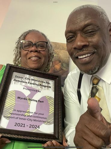 Two people smiling, one holding a framed appreciation certificate.