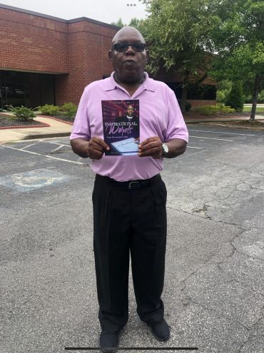 Man in sunglasses holding a book outdoors in a parking lot.