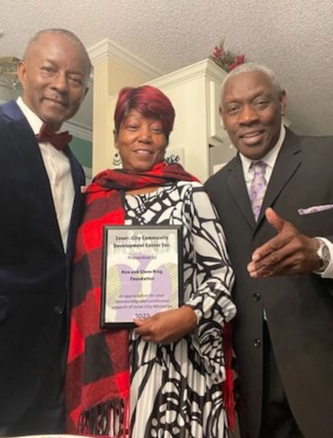 Three people posing, woman in center holding an award plaque.