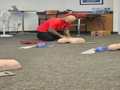 A man practices CPR on a training dummy in a classroom setting.