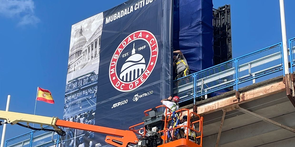 Workers setting up Mubadala Citi DC Open banner on a stadium.