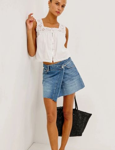Woman wearing a white sleeveless top and denim skirt, carrying a black woven bag.