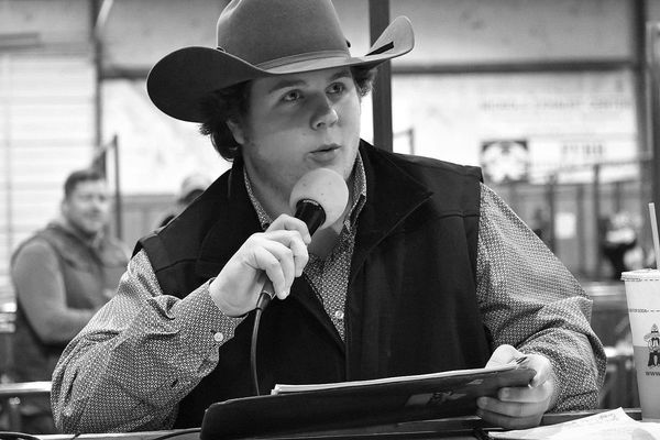 A man in a cowboy hat speaks into a microphone while holding papers.