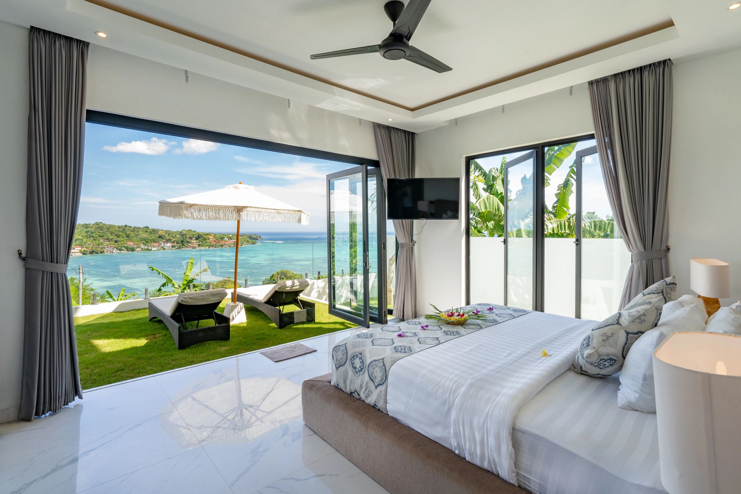 Modern bedroom with ocean view and outdoor lounge area.