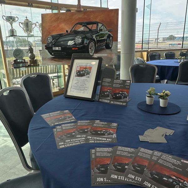 Art display featuring a classic black car painting and promotional flyers on a blue tablecloth.