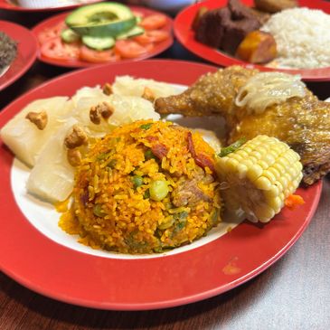 A plate of jollof rice, fried chicken, corn, and yam on a red-bordered plate.
