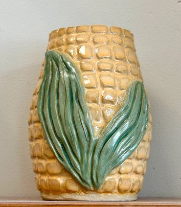 Ceramic vase shaped like an ear of corn with green leaves.