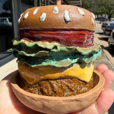 A realistic ceramic sculpture of a cheeseburger with lettuce and tomato.