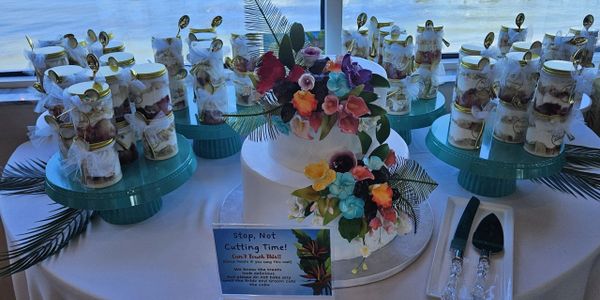 Decorative wedding cake surrounded by individual dessert parfaits on a table.
