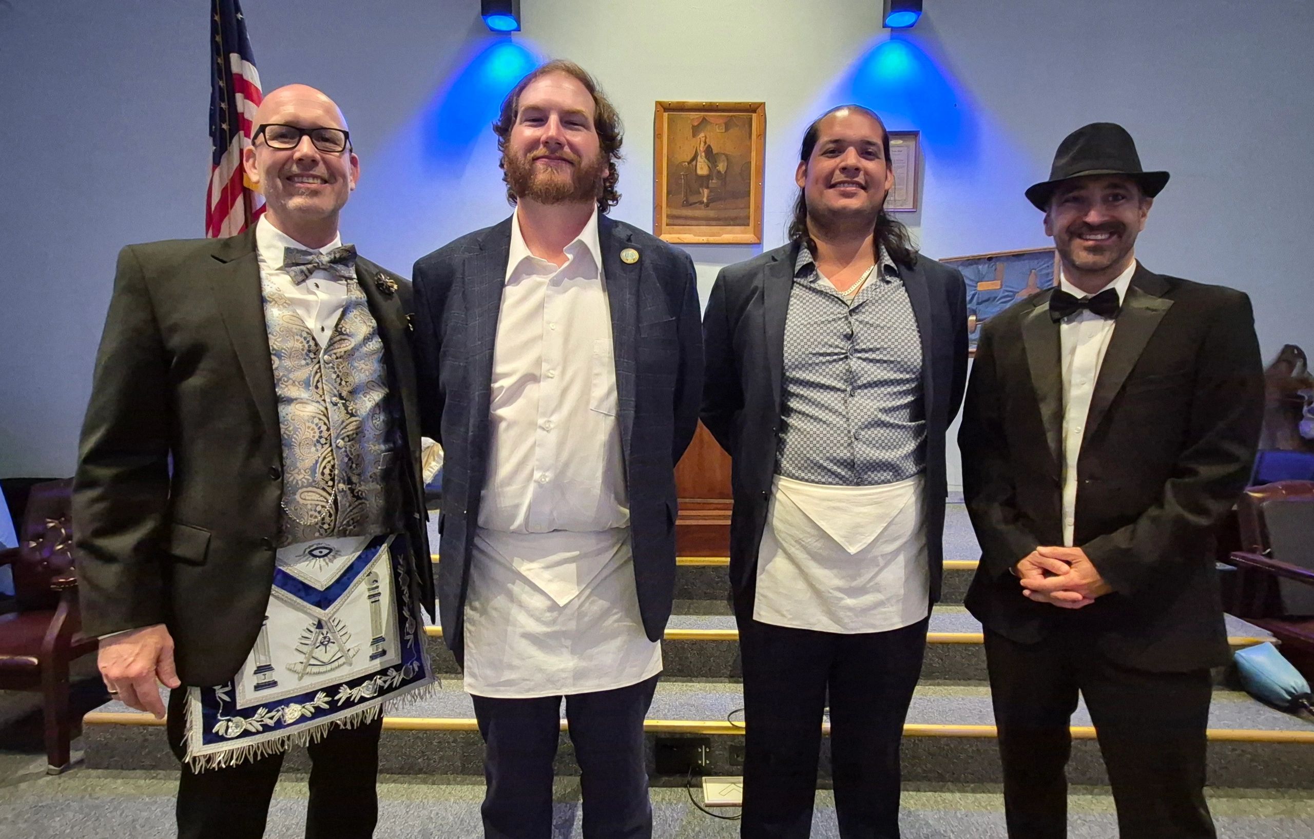 Four men in formal attire with aprons, standing in a ceremonial setting.