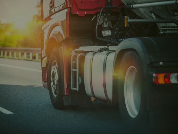 Close-up of a red truck driving on a highway at sunset.