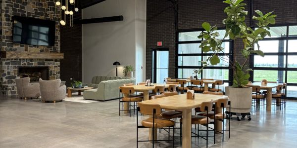 Spacious modern lounge with wooden tables, cozy seating, and large windows letting in natural light.