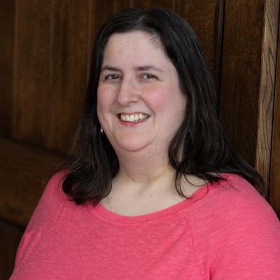 Woman smiling in a pink top near a wooden wall.