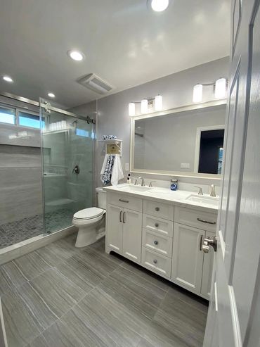 remodeled  bathroom. Shower, toilet, white cabinets, big mirror