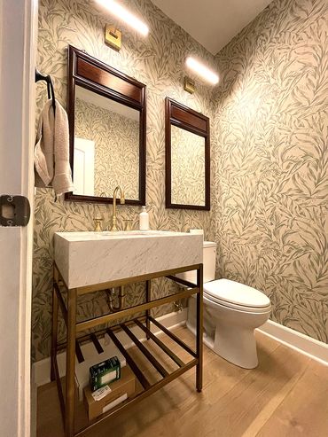 Renovated bathroom. Modern sink, toilet and white wallpaper with green leaves