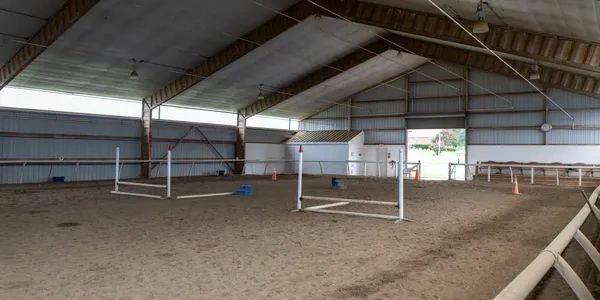 Indoor equestrian arena with jumping obstacles and sandy floor.