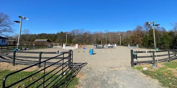 Empty outdoor horse riding arena with fences and jumps under clear blue sky.