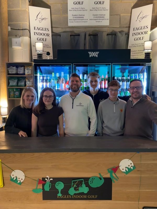 Group of six people smiling behind a bar at Eagles Indoor Golf venue.
