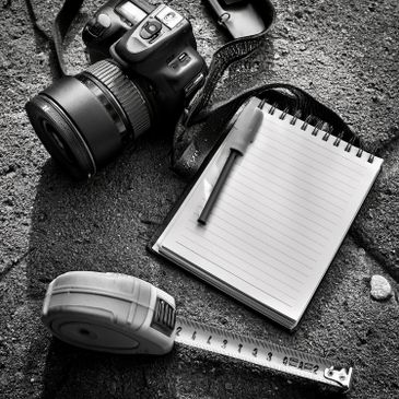 Camera, notebook with pen, and measuring tape on textured surface.