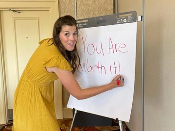 woman writing "You are worth it!" on a flip chart.