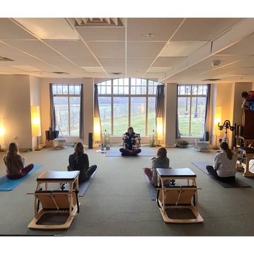 four folks sitting on yoga mats looking at one person in the front of a room 