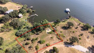 A lakeside property outlined in red with trees, a fire pit, and docks nearby.
