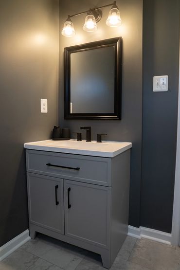 Modern bathroom vanity with a mirror, dark walls, and overhead lighting.