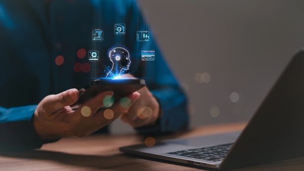 Hands holding a phone with an AI head and icons floating above it.