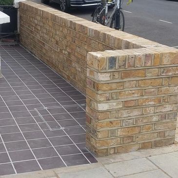 yellow brick front garden wall with a black tiled exterior flooring in London