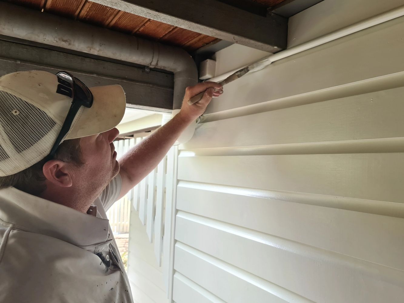 A man painting the exterior wall of a house with a brush.