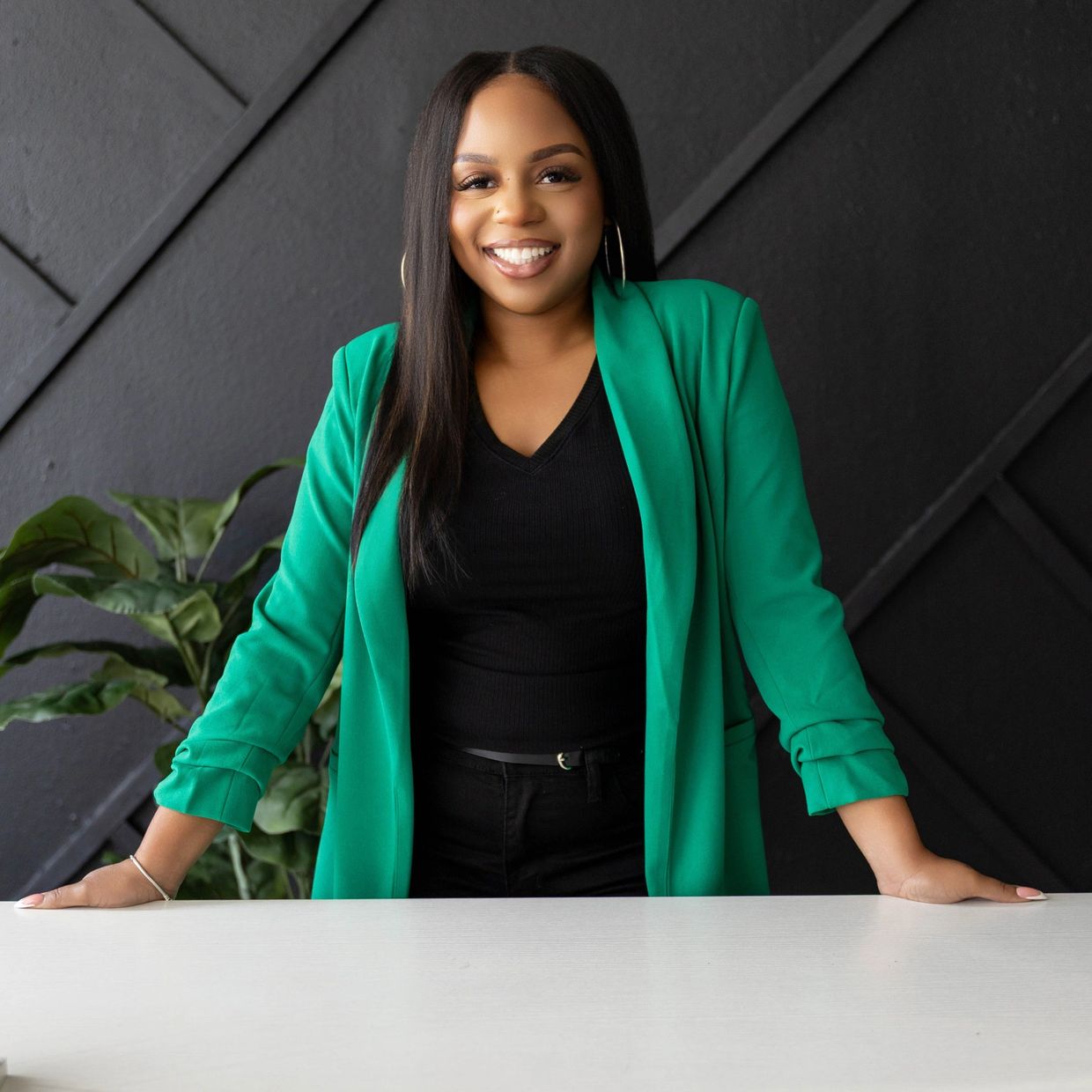 Confident woman smiling, wearing green blazer and black top.