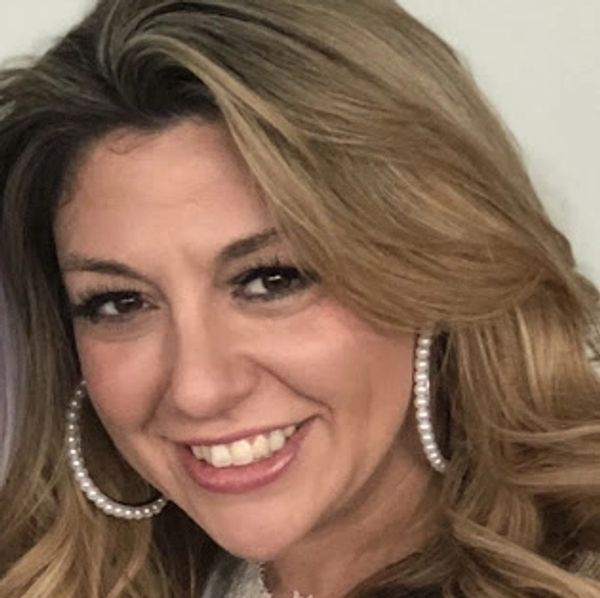 Woman smiling with blonde hair and large pearl hoop earrings.
