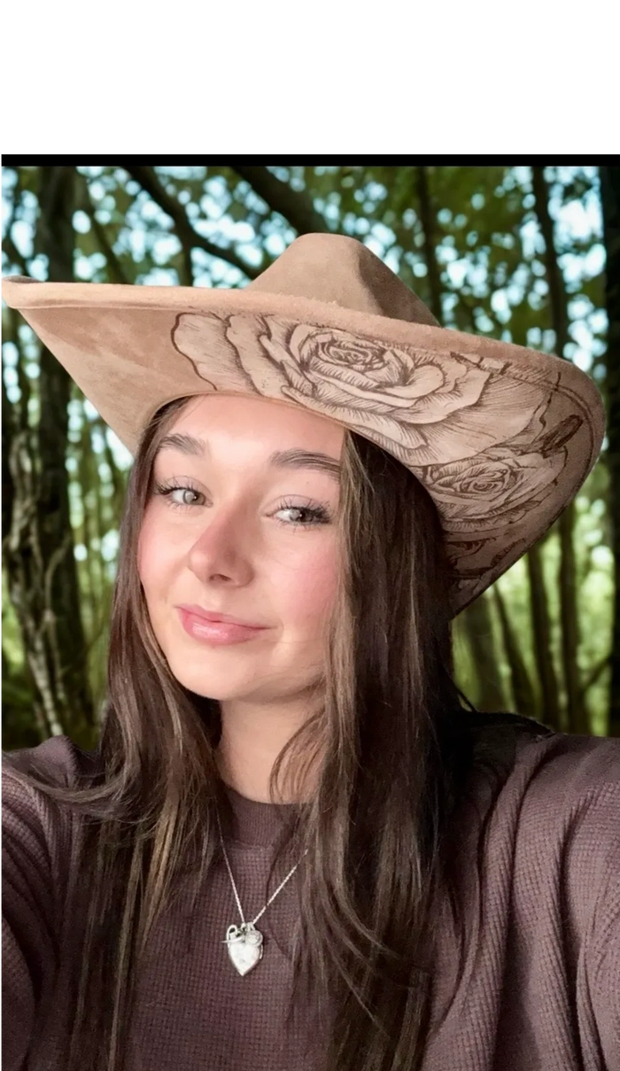 Young woman wearing a floral cowboy hat and a purple sweater in a forest setting.