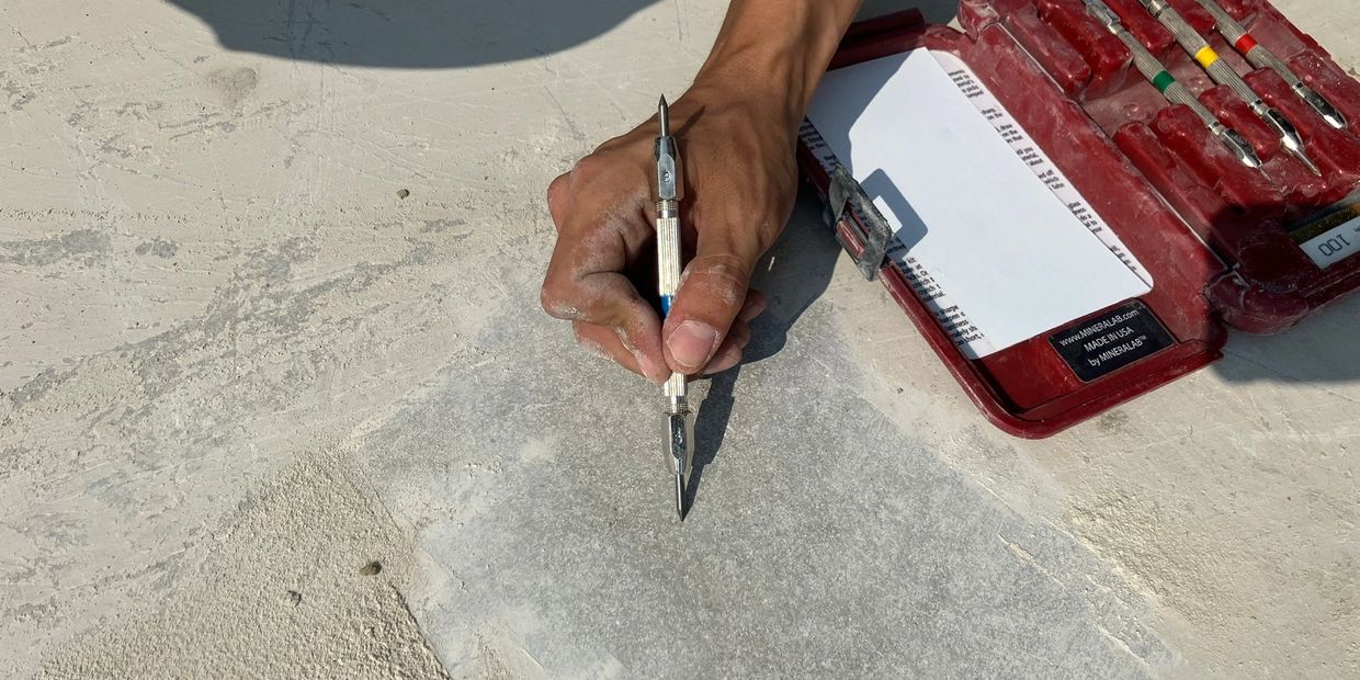 Hand holding a stone carving tool near a red toolcase on a stone surface.