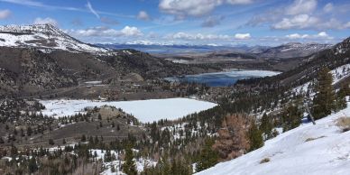 Snowy mountain valley with lakes and trees under a blue sky.
