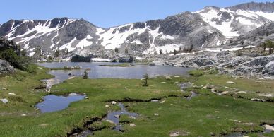 Mountain lake with snow patches and green meadow.