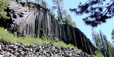 Basalt columns in a forested area under a clear blue sky.