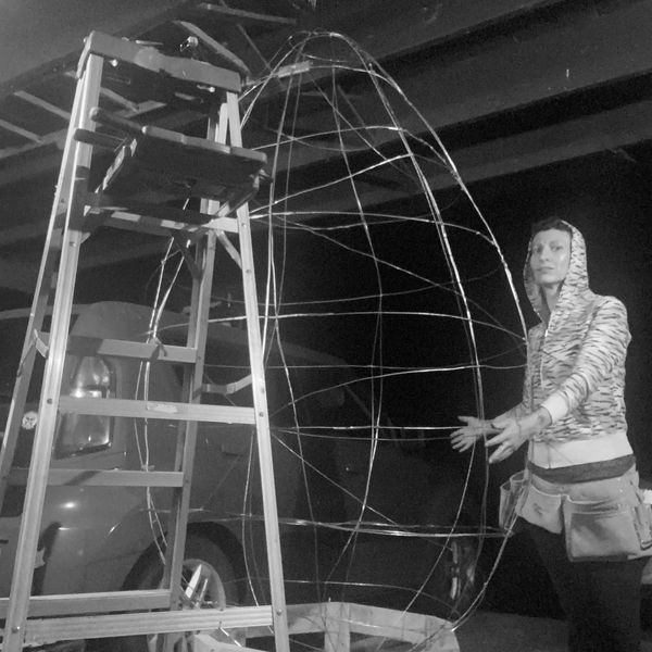 Person standing next to a large wire frame and ladder.