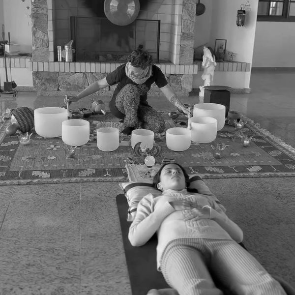 Person playing crystal singing bowls while another person relaxes.